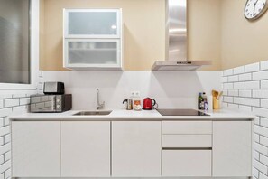 A modern kitchen with white cabinets, a stainless steel sink, a microwave, a red coffee maker, and a clock on the wall. - The Collection - Arc de Triomf Modern 2BD 2BTH (Barcelona)