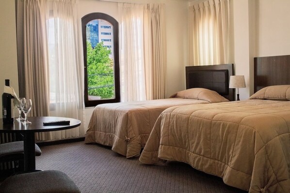 Ein Hotelzimmer mit zwei Betten, einem runden Tisch, einem Stuhl und Blick auf Grün durch das Fenster.