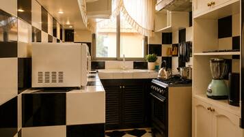 A compact kitchen with a black and white checkered floor, a stove, a kettle, a blender, and a refrigerator.