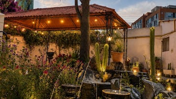 Un giardino con fontana, cactus e zona relax coperta.
