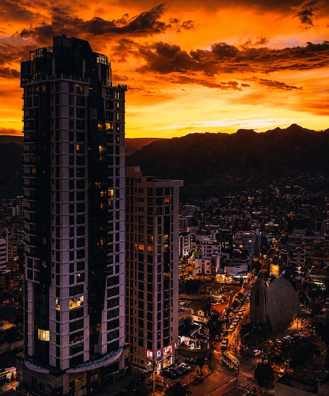 Une vue d’une ville au crépuscule, avec des gratte-ciel et une chaîne de montagnes en arrière-plan.