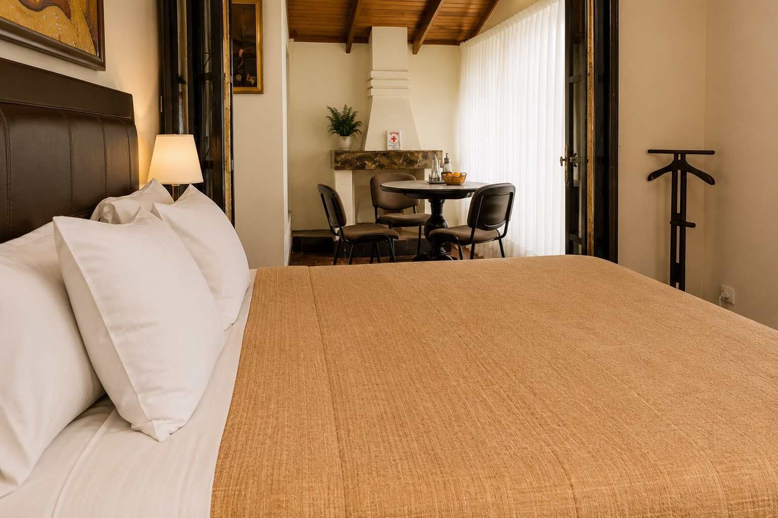 Une chambre d’hôtel avec un grand lit, un bureau avec des chaises, une lampe et une plante.