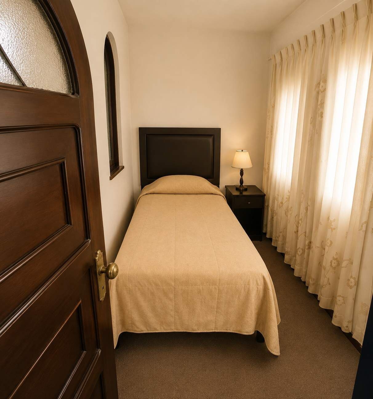 Ein Hotelzimmer mit einem Bett, einem Nachttisch mit Lampe, einer Tür und Vorhängen.