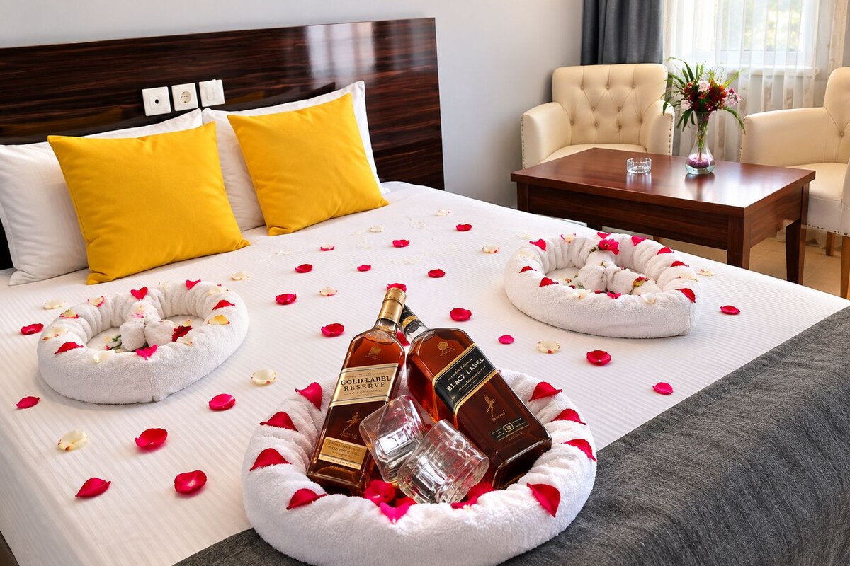 A hotel room with a neatly made bed, two yellow pillows, a wooden headboard, a bedside table with a vase of flowers, and a chair.