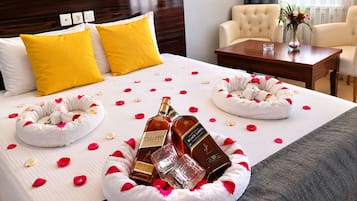 A hotel room with a neatly made bed, two yellow pillows, a wooden headboard, a bedside table with a vase of flowers, and a chair.