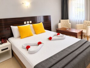 Una habitación de hotel con cama, mesita de noche, lámpara y un área de descanso con sillas y mesa.