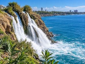 Una cascada costera con vista al océano y un horizonte urbano de fondo.