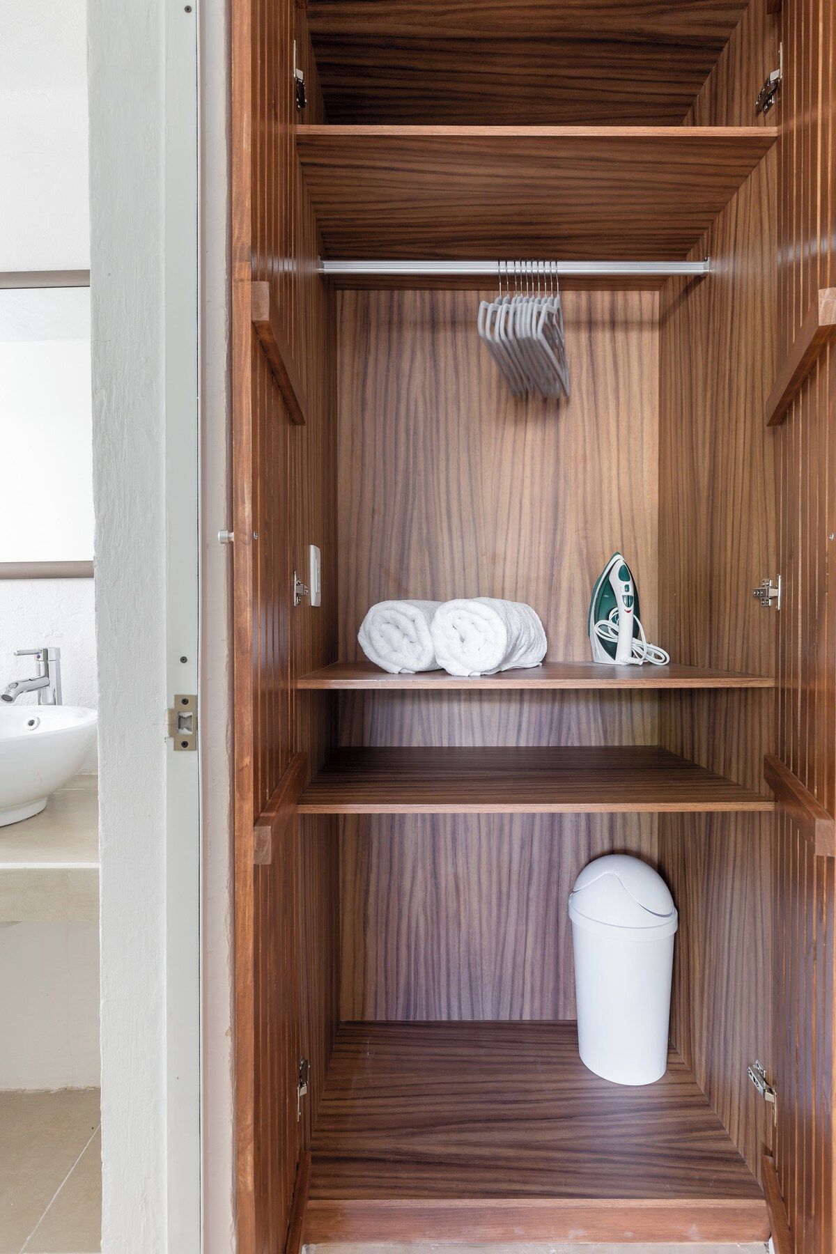 A wooden wardrobe with multiple shelves, a hanging rack, and a trash bin.