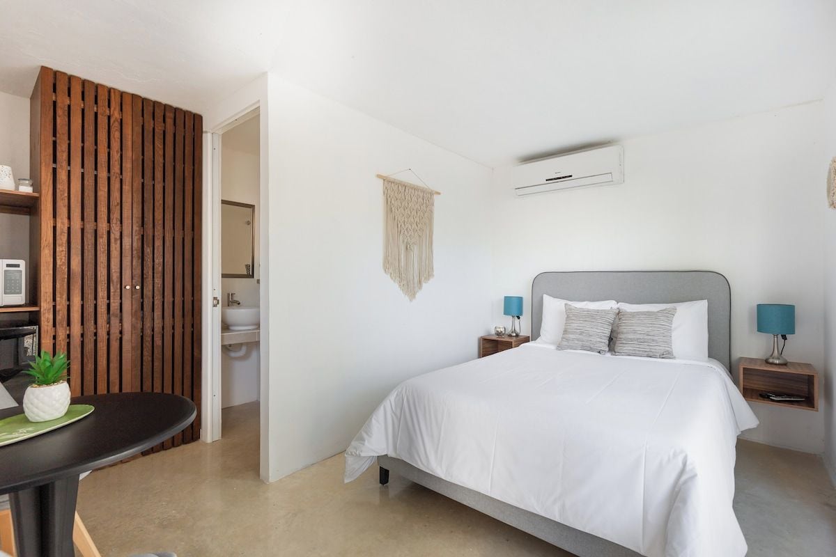 Quarto com cama, mesas de cabeceira, ar condicionado fixado na parede e um painel de madeira.