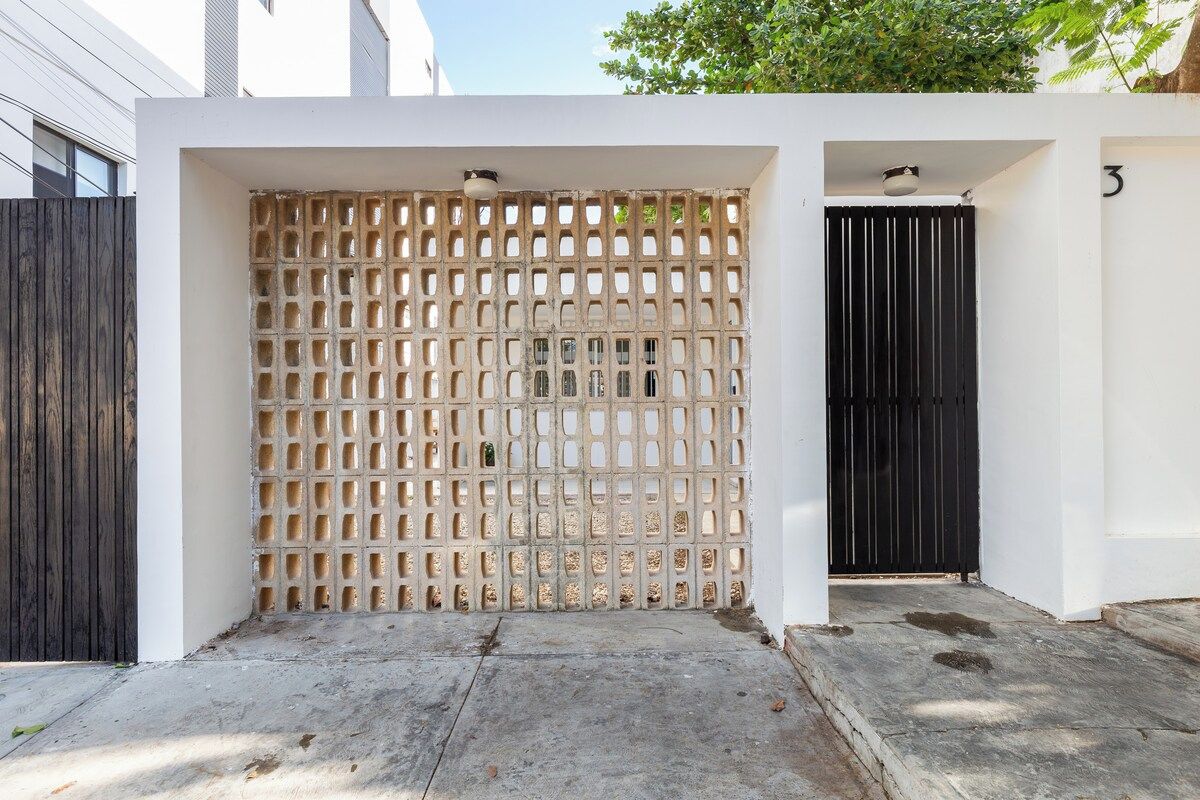 A gated entrance with a wooden lattice fence, a black gate, and a concrete pathway leading to a building.
