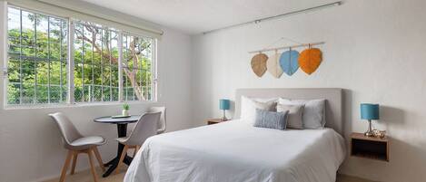 A bedroom with a bed, two chairs, a small table, and a window with a view of trees.