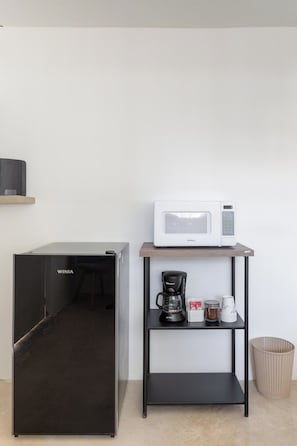 Geladeira preta e micro-ondas em uma prateleira com cafeteira e recipientes.