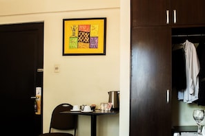 A room with a dining table, chairs, a framed artwork, a coat rack, and a wardrobe.