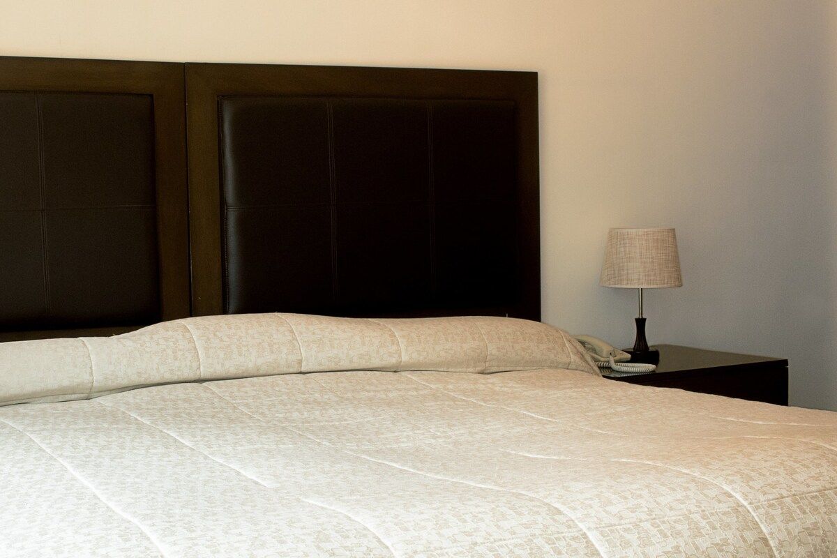 A bed with a headboard, a bedside table with a lamp, and a wall.