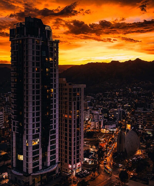 A cityscape at dusk with high-rise buildings and a mountain range in the background.