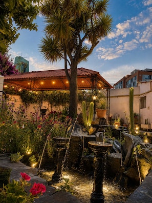 A garden with a fountain, cacti, and a covered seating area. - Calacoto Suite | Garden + 24/7 Concierge (La Paz)