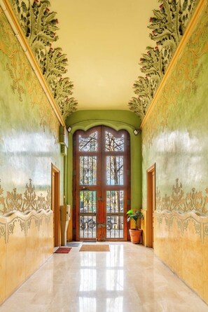 Un couloir avec un mur vert, une porte en bois dotée de panneaux de verre et une plante en pot.