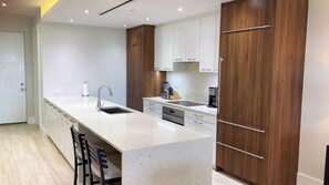 A modern kitchen with a central island, white cabinetry, and a wooden accent wall. - 5th Floor Condo at ONE Cable Beach (Nassau)