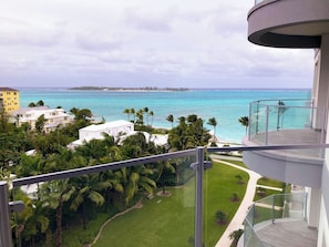 A high-rise building with a balcony overlooking a coastal area with palm trees and a clear view of the ocean. - 5th Floor Condo at ONE Cable Beach (Nassau)