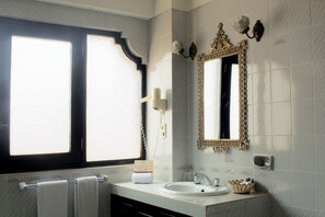 A bathroom with a large window, a sink, a mirror with an ornate frame, and a towel rack.
