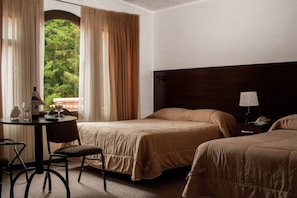 Ein Hotelzimmer mit zwei Betten, einem Esstisch, einem Stuhl und Blick auf Grünflächen.