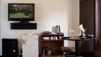 A compact hotel room with a television, a small refrigerator, a dining table with a chair, and a cabinet.