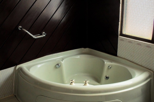 A corner bathtub with a wooden panel wall and a window.