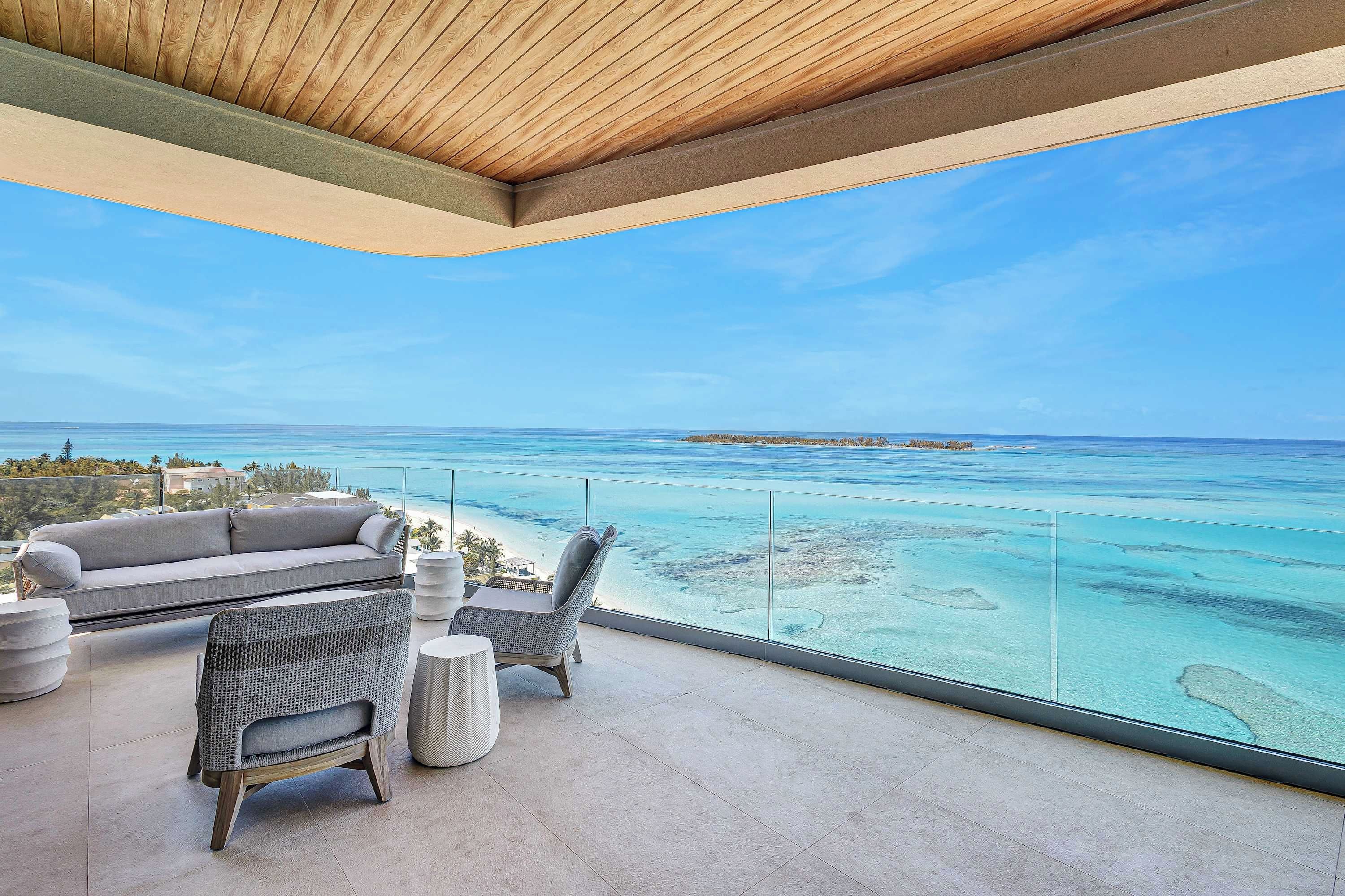 A balcony with a view of the ocean, a sofa, and two chairs.