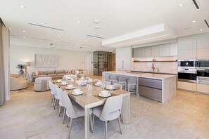 A modern kitchen with a central island, a dining area with a long table, and a living area with a sofa. - Oceanfront Aqualina Penthouse with Infinity Pool (Nassau)