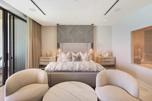 A modern bedroom with a large bed, two nightstands, a round coffee table, and a view of the outside. - Oceanfront Aqualina Penthouse with Infinity Pool (Nassau)