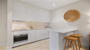 A modern kitchen with white cabinetry, a built-in oven, a sink, and a round woven wall hanging. - Penthouse with Ocean Views and Infinity Pool (Nassau)