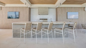 A modern bar area with a long counter, five wicker chairs, and two wall-mounted TVs. - Penthouse with Ocean Views and Infinity Pool (Nassau)