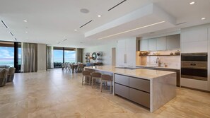 Uma cozinha moderna com uma ilha central, banquetas de bar e vista para o oceano.