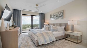 A modern bedroom with a large bed, a flat-screen TV, a ceiling fan, and a city view. - Penthouse with Ocean Views and Infinity Pool (Nassau)