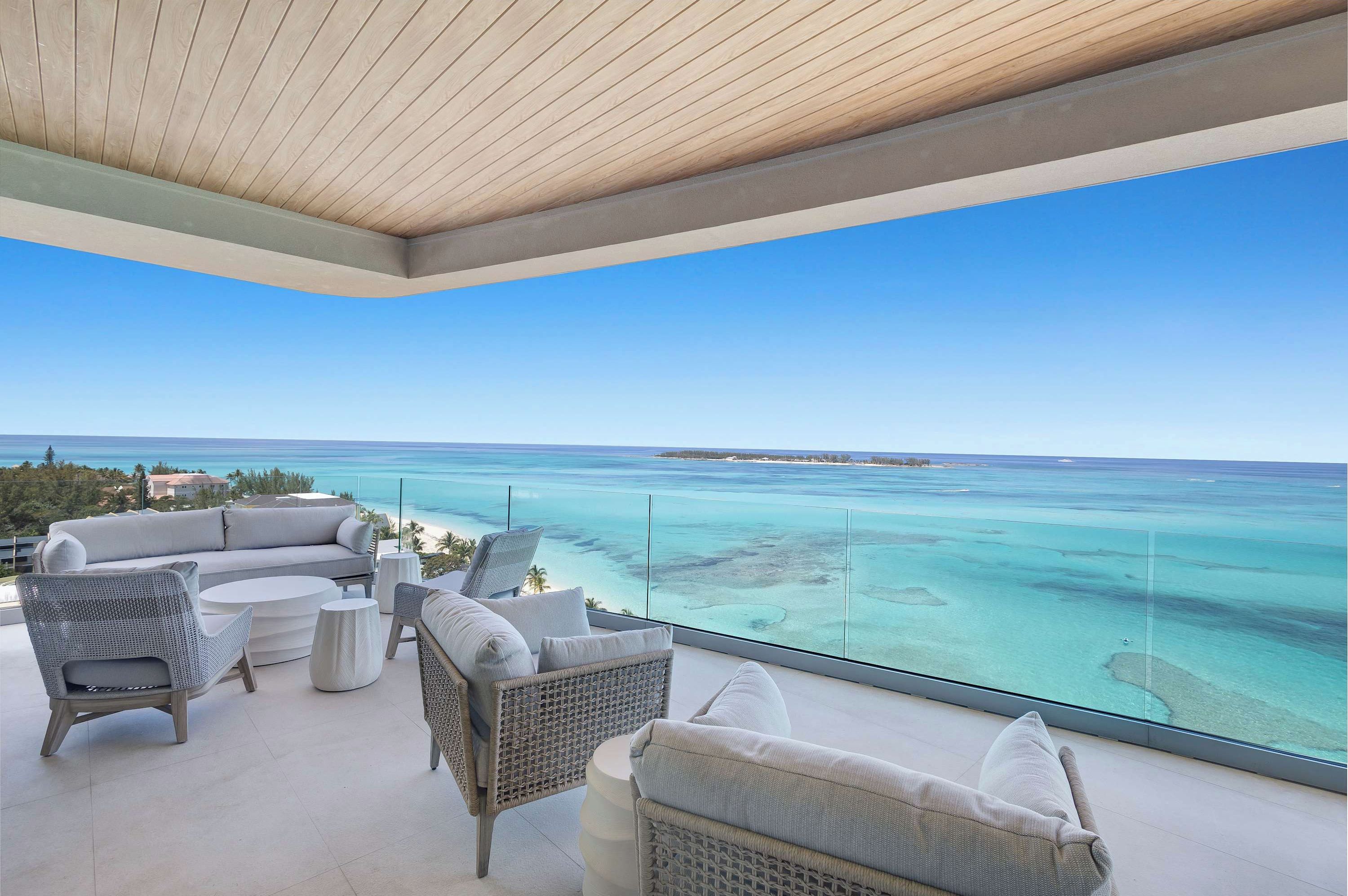A balcony with a view of the ocean, wicker furniture, and a glass railing.