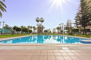 A swimming pool with a clear blue water surface, surrounded by palm trees and a fence. - Seafront Apartment with Parking (Almuñécar)