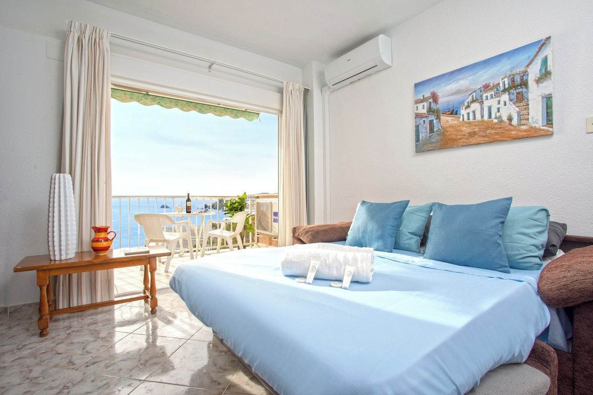 Une chambre d'hôtel avec un lit, une table avec une carafe, une chaise et un balcon avec vue.