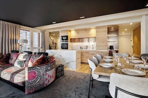 A modern living room with a sofa, a dining table set for a meal, and a kitchen area with a marble countertop. - Luxurious Apartment with Ski-In and Out Access in Centre (Toulouse)