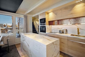 A modern kitchen with a marble countertop, wooden cabinets, and a built-in oven. - Luxurious Apartment with Ski-In and Out Access in Centre (Toulouse)