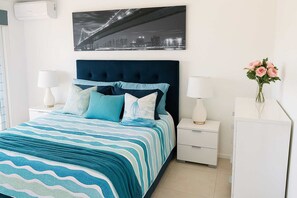 A bedroom with a bed, nightstands, a dresser, a wall-mounted air conditioner, and a framed picture above the bed. - 2 Bedroom Apartment near The Strand with Parking in Townsville (North Ward)