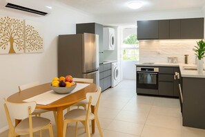 A modern kitchen with a dining area, stainless steel appliances, and a fruit bowl on the table. - 2 Bedroom Apartment near The Strand with Parking in Townsville (North Ward)