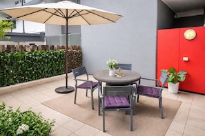 A round table with four chairs, a beige umbrella, and a potted plant. - Townsville CBD Stadium 2BR, 2BA w Pool, Spa & Parking (Townsville City)