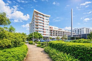 A modern multi-story hotel with a central courtyard, surrounded by lush greenery and a clear blue sky. - CBD Balcony, Stadium & V8 Views & 2 Car Parks (Townsville City)