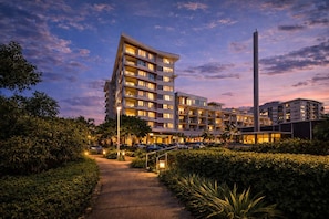 A multi-story hotel with a modern design, featuring balconies on each floor, a central pathway, and a tall structure to the right. - CBD Balcony, Stadium & V8 Views & 2 Car Parks (Townsville City)
