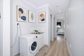 A laundry area with a washing machine, a sink, and a small plant. There are three framed artworks on the wall. - Townsville Golf Course Duplex 2 Bed 2 Bath w Secure Parking (Johannesburg)