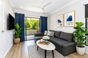 A modern living room with a grey sofa, a coffee table, a TV, and a balcony with blue curtains. - Townsville Golf Course Duplex 2 Bed 2 Bath w Secure Parking (Johannesburg)