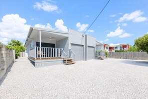 Uma casa moderna com varanda coberta, entrada por um caminho de cascalho e cerca de madeira.