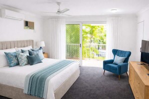 A bedroom with a bed, a chair, a TV, and a balcony with a view of palm trees. - Beachside 2BR Apartment Townsville 1 Min Walk to The Strand w Parking (North Ward)