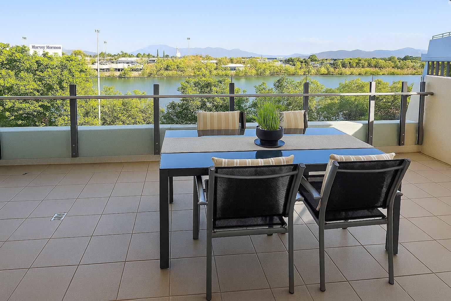 Una terraza con mesa y sillas, una planta en maceta y vistas a un lago y montañas distantes.