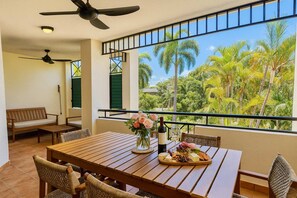 A balcony with a wooden table set for dining, featuring a bottle of wine, a glass, and a fruit platter. - Townsville Waterfront Apartment with 2 BR Pool & Parking (Townsville City)